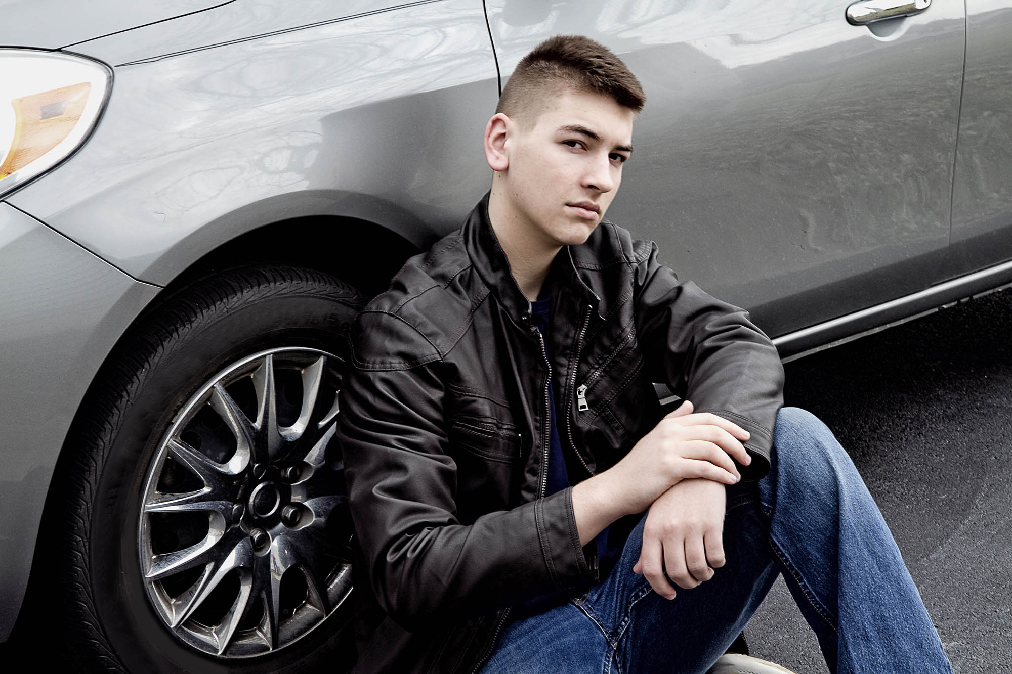 Teen boy sitting down by his car